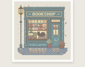 May include: A cross-stitch pattern featuring a teal bookstore storefront with the word BOOKSHOP above the window. The design includes a black cat in the window, a tall street lamp, potted plants, and a cobblestone sidewalk with scattered leaves.