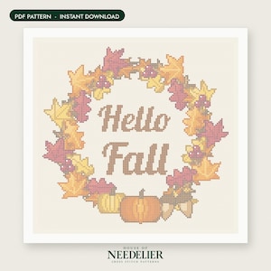 May include: A cross stitch pattern featuring a wreath of autumn leaves in shades of yellow, orange, and pink, surrounding the brown text "Hello Fall". At the bottom, there are two pumpkins and two acorns. The design is on a light cream grid background.