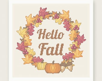 May include: A cross stitch pattern featuring a wreath of autumn leaves in shades of yellow, orange, and pink, surrounding the brown text "Hello Fall". At the bottom, there are two pumpkins and two acorns. The design is on a light cream grid background.