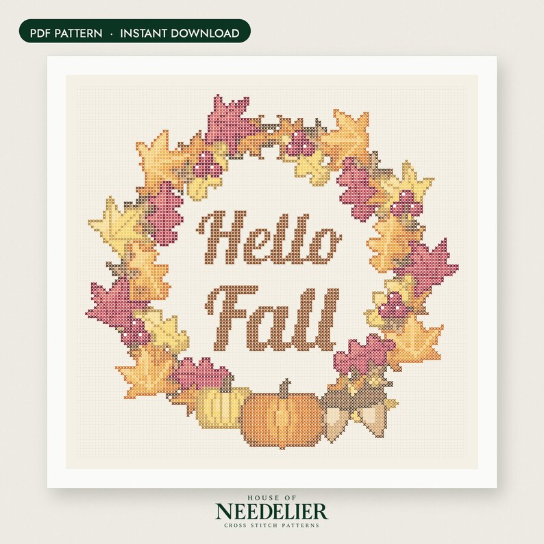 May include: A cross stitch pattern featuring a wreath of autumn leaves in shades of yellow, orange, and pink, surrounding the brown text "Hello Fall". At the bottom, there are two pumpkins and two acorns. The design is on a light cream grid background.