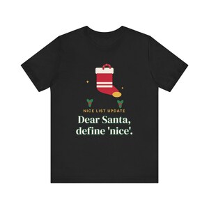 May include: A black short-sleeve t-shirt featuring a graphic of a red and white Christmas stocking, two small green sprigs, and the text "NICE LIST UPDATE" in yellow followed by "Dear Santa, define 'nice'." in white serif lettering.