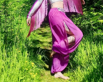 May include: A woman wearing a pink and silver costume with a flower crown, standing in a grassy area with trees in the background.