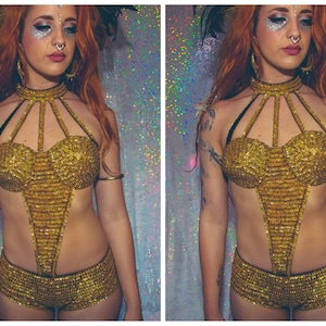 K&ouml;nnte beinhalten: Ein goldenes, paillettenbesetztes zweiteiliges Outfit mit einem Halstuch und Shorts. Das Outfit hat ein geometrisches Design und wird von einer Person mit roten Haaren und Make-up getragen.