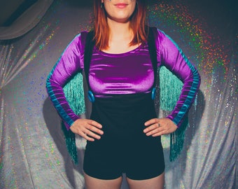 Könnte beinhalten: Ein Oberteil aus lila Samt mit schwarzen Shorts und türkisfarbenem Fransenbesatz. Das Outfit wird von einer Person mit roten Haaren getragen.