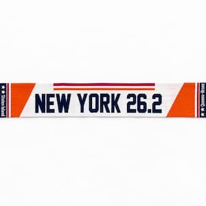 May include: A knit scarf featuring orange, white, and blue colors with the text NEW YORK 26.2 in dark blue. The ends have fringe, and the design includes the names Staten Island, Brooklyn, Queens, Bronx, and Manhattan with stars.