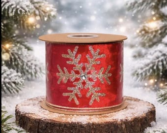 May include: A spool of red ribbon featuring a repeating gold glitter snowflake pattern with a central clear rhinestone accent on each snowflake. The ribbon has a metallic finish and is wound around a circular cardboard core with finished edges.