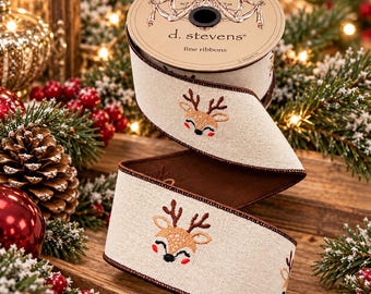 May include: A spool of beige ribbon with a dark brown edge, featuring an embroidered reindeer face pattern. The spool is labeled d. stevens fine ribbons. The ribbon has a textured fabric appearance and displays a repeating design of a smiling deer.