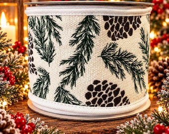 May include: A wide spool of cream-colored fabric ribbon featuring a repeating pattern of dark green pine needles and brown pinecones. The ribbon has a textured weave and finished edges, designed for decorative use in holiday arrangements.