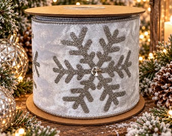 May include: A spool of light gray velvet ribbon featuring a large, centered silver glitter snowflake design. The snowflake has a small, clear, faceted crystal accent at its center. The ribbon edges are finished with a thin, metallic silver trim.