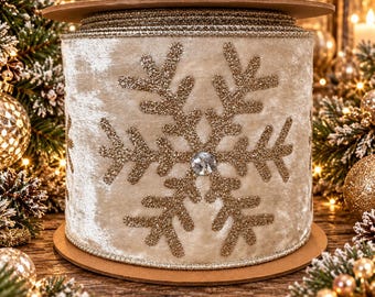 May include: A spool of wide, champagne-colored velvet ribbon featuring a repeating pattern of large, glittery gold snowflakes. Each snowflake is centered with a single, clear, faceted crystal accent. The ribbon edges are finished with gold trim.