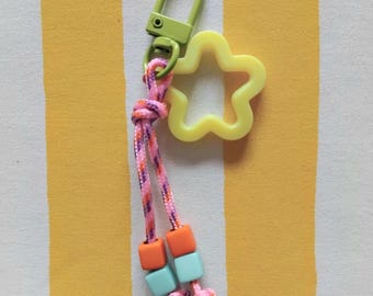 May include: A lime green star-shaped keychain with a lime green metal clasp and a pink, orange, and purple braided cord with turquoise and orange square beads.
