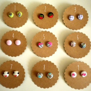 May include: Nine sets of fabric covered button earrings displayed on brown card circles numbered 1 to 9. The earrings are in various colours and patterns, including pink, blue, red, green, and floral.