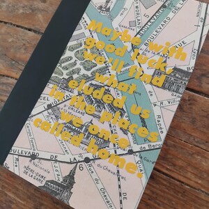 May include: A notebook featuring a map design with the text "Maybe good luck will find us once we're on places called home" in yellow. The notebook has a black spine and a light pink and green map cover.