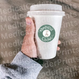 Puede incluir: Un vaso de café desechable blanco con tapa de plástico translúcido. El vaso presenta un logotipo circular de color verde salvia con el texto Medical Coder y una pequeña ilustración lineal de una taza humeante con un corazón.