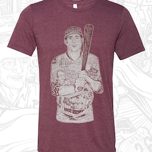 May include: A maroon t-shirt with a white graphic print of a baseball player holding a bat. The graphic includes the text "PHILLY", "STAR", "26", "1008", "BROAD", "01", "2008", "UTLEY", "CHAMPIONS", "SENILS-35GAME HITTIN", "AND SEAM", "SLUGGER".