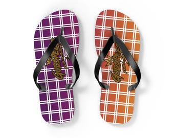 May include: A pair of flip-flops featuring black rubber straps and a grid pattern. The left sandal is purple with white lines, and the right is orange with white lines. Both display a gold crown icon and the text GODSPEED Faith in Motion.