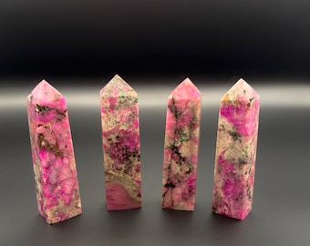 May include: Four upright crystal towers with pointed tops, featuring a vibrant mix of magenta, white, and grey mineral inclusions. Each stone column displays a unique, natural pattern of deep pink crystalline structures contrasted by dark grey and white matrix veins.