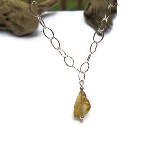 May include: A silver chain necklace with a teardrop-shaped yellow gemstone pendant.