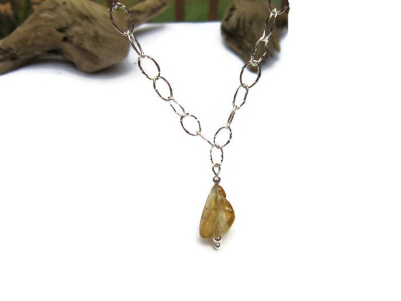 May include: A silver chain necklace with a teardrop-shaped yellow gemstone pendant.
