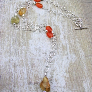 May include: A silver chain necklace with orange and yellow gemstone beads. The necklace has a toggle clasp and a long, dangling pendant.