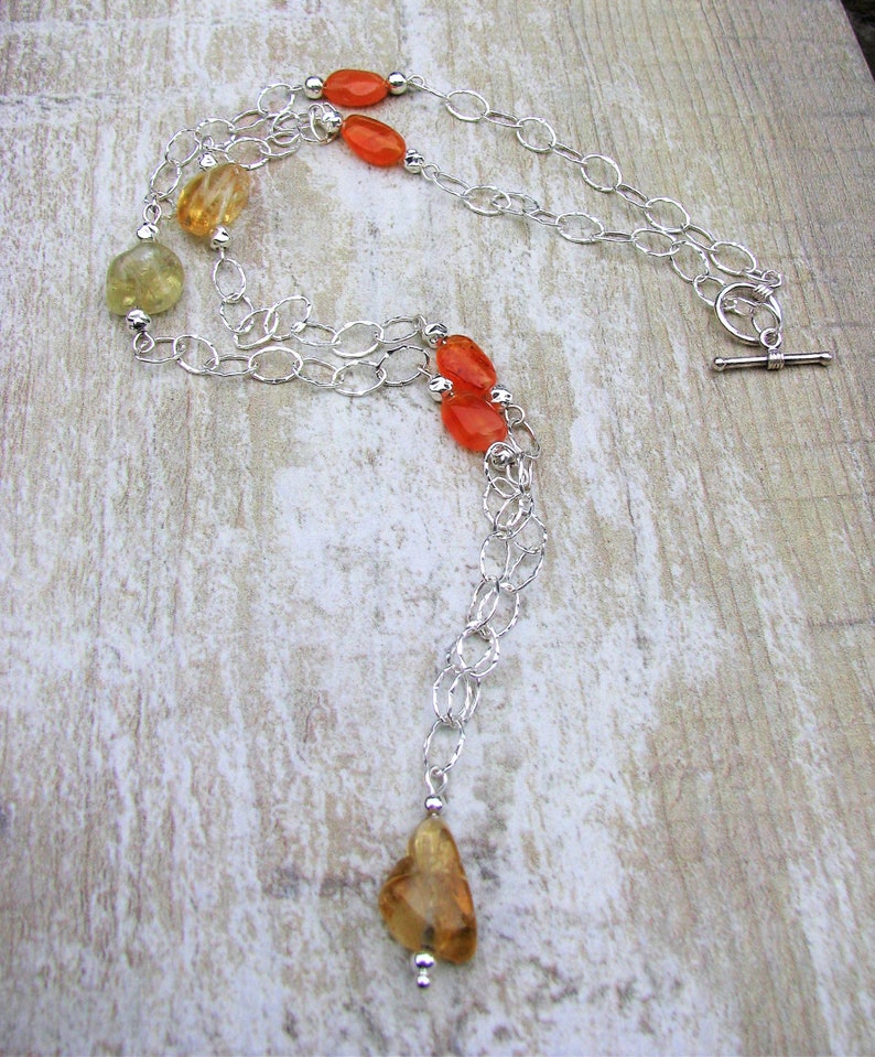 May include: A silver chain necklace with orange and yellow gemstone beads. The necklace has a toggle clasp and a long, dangling pendant.