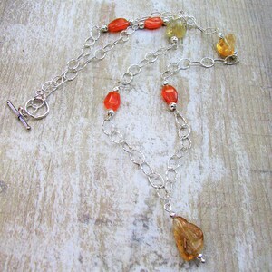 May include: A silver chain necklace with orange and yellow gemstone beads. The necklace has a lobster clasp and a small pendant.