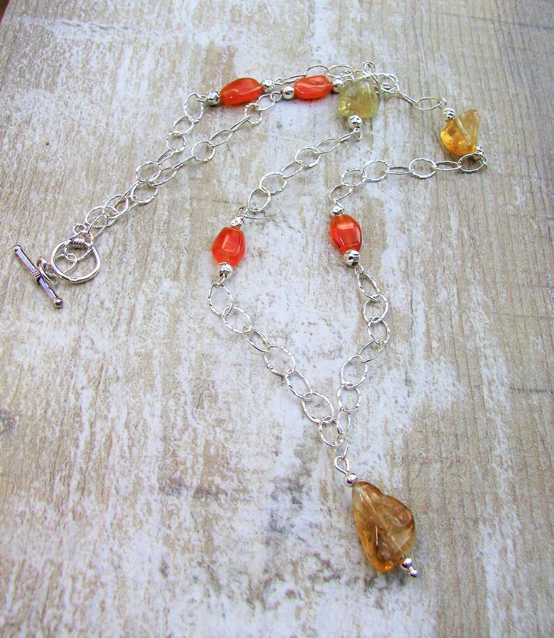May include: A silver chain necklace with orange and yellow gemstone beads. The necklace has a lobster clasp and a small pendant.
