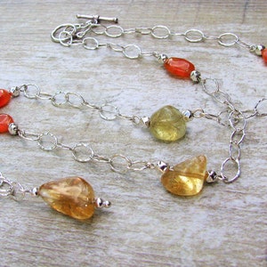 May include: A silver chain necklace with carnelian and citrine gemstones. The necklace has a lobster clasp closure.