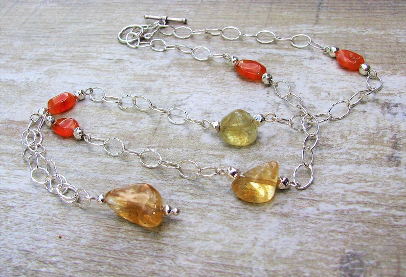 May include: A silver chain necklace with carnelian and citrine gemstones. The necklace has a lobster clasp closure.