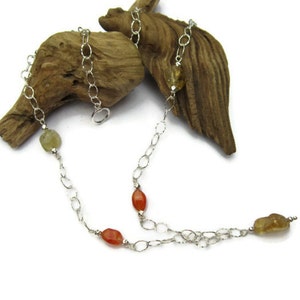 May include: A silver chain necklace with carnelian and citrine gemstones. The necklace is displayed on a piece of driftwood.
