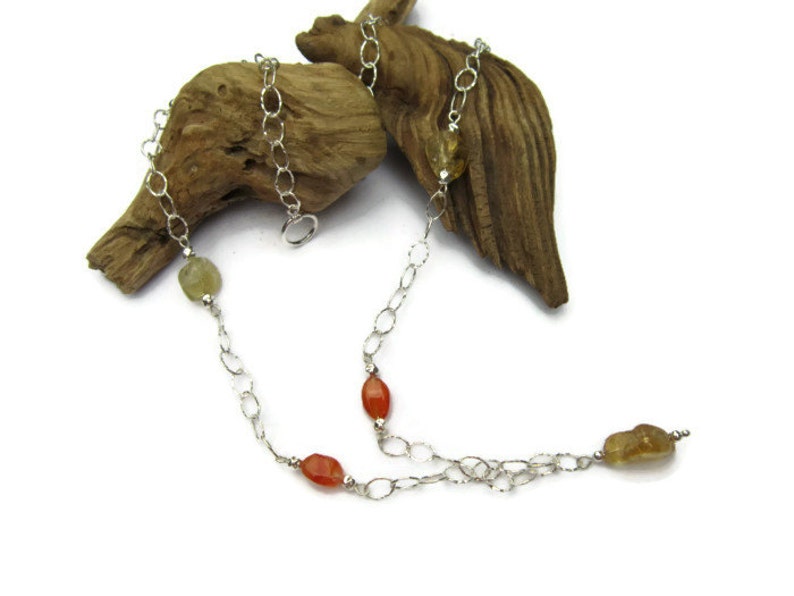May include: A silver chain necklace with carnelian and citrine gemstones. The necklace is displayed on a piece of driftwood.