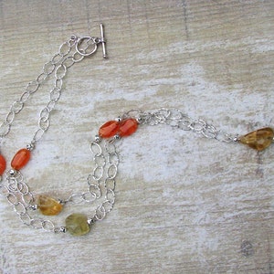May include: A silver chain necklace with orange and yellow gemstone beads. The necklace has a toggle clasp.