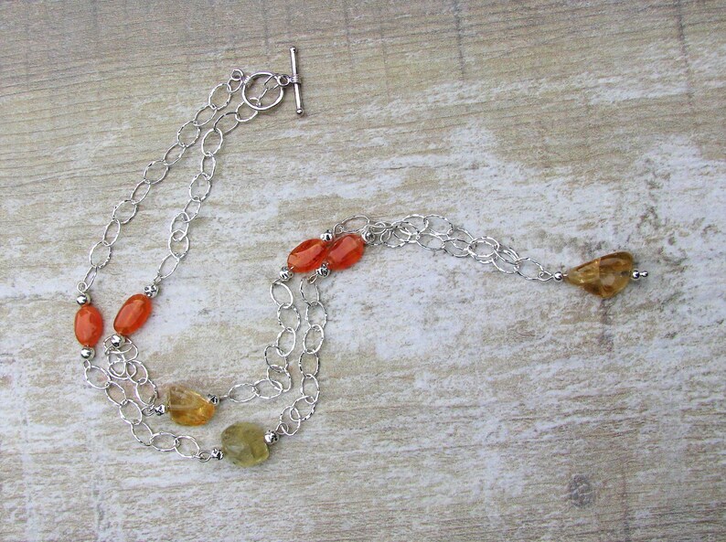 May include: A silver chain necklace with orange and yellow gemstone beads. The necklace has a toggle clasp.