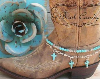 May include: A tan leather cowboy boot adorned with a multi-strand anklet featuring turquoise-colored beads, clear crystals, and silver-toned chain links with dangling turquoise cross charms. The text Boot Candy is visible on the boot shaft.