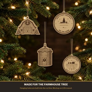 May include: Four light-coloured wooden Christmas ornaments hanging by strings. Designs include a barn, a grain silo, and two circular ornaments with text reading Baby's First Christmas On The Farm 20 and Home For Christmas Down The Gravel Road.