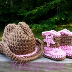 May include: A brown crochet cowboy hat and matching baby boots with pink accents. The boots feature a star design. The items are handmade and suitable for a baby. The word "KrazyHat" is written in pink.