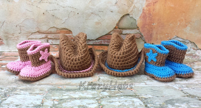 May include: A collection of crocheted cowboy hats and boots in pink, brown, and blue. The boots feature star accents. The hats and boots are arranged in a row against a rustic brick background. The text "KrazyHats" is visible.