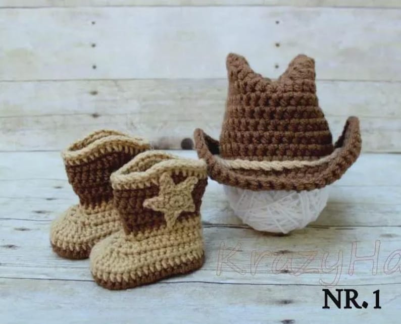 May include: A crochet set featuring a cowboy hat and boots in shades of brown and tan. The boots have a star applique. The hat is perched on a ball of white yarn. The text "KrazyHa" and "NR.1" are visible.