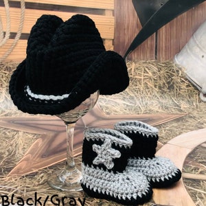 May include: A black crochet cowboy hat with a white and gray band sits atop a wine glass. Matching black and gray crochet baby cowboy boots with a star design are in front of the glass. The text "Black/Gray" is at the bottom.
