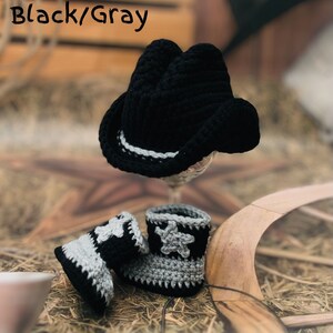 May include: A black and gray crochet cowboy hat and matching baby boots. The hat has a white and gray band. The boots have a star design. The text "Black/Gray" is in the upper left corner.
