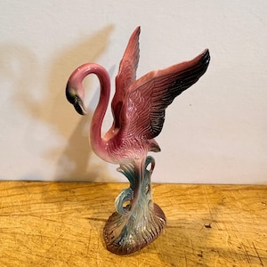 Estatueta vintage de flamingo rosa em cerâmica com asas abertas.