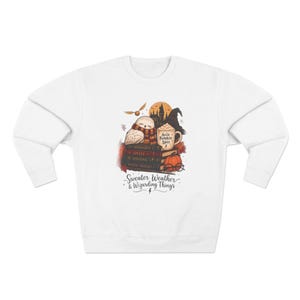 May include: A white long-sleeve sweatshirt featuring a graphic of an owl wearing a scarf, a mug labelled Accio Pumpkin Spice, books, a pumpkin, and glasses. The text reads Sweater Weather & Wizarding Things with a small lightning bolt icon below.