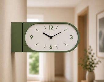 May include: A double-sided wall clock with an olive green frame and a white face. The clock features dark green numerals at the 12, 3, 6, and 9 positions, with simple black hour and minute hands and thin black tick marks for the remaining hours.