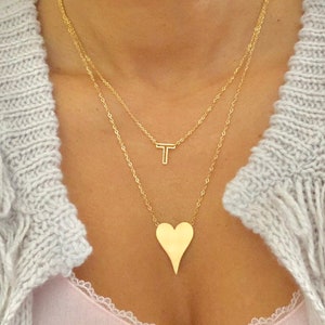 May include: A gold layered necklace with a heart pendant and a letter T pendant.