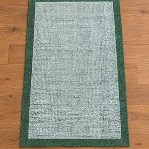 Puede incluir: Una alfombra rectangular que presenta un panel central texturizado de color azul claro rodeado por un borde sólido de color verde bosque oscuro. La alfombra tiene una apariencia tejida con un patrón consistente en toda la sección azul claro y un acabado plano y uniforme en el marco verde oscuro.