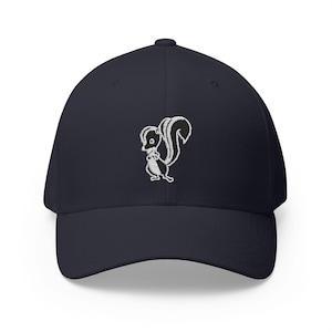 May include: A navy blue baseball cap featuring a white embroidered graphic of a small skunk standing on its hind legs. The cap has a structured crown, a curved brim, and a button on top, showcasing a clean and simple design on the front panel.