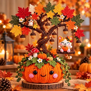 Puede incluir: Un árbol de otoño tejido a ganchillo con una base de calabaza naranja sonriente, un gato en un columpio, un pájaro pequeño, bellotas colgantes, setas rojas y blancas y hojas de arce coloridas iluminadas por pequeñas luces blancas cálidas.