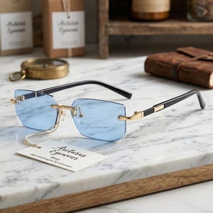 May include: Rimless glasses featuring light blue rectangular lenses, a gold-tone metal bridge, and black temples. A white rectangular tag attached to the bridge displays the text Arcturus Eyewear Etsy etsy.com/shop/ArcturusEyewear.