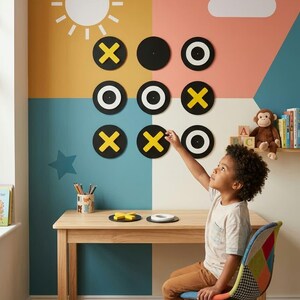 May include: A wall-mounted tic-tac-toe game featuring nine circular black discs with yellow X and white O symbols. The game is displayed on a multi-colored wall with a sun and cloud graphic, positioned above a light-colored wooden table and chair.