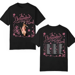 May include: A black short-sleeve t-shirt featuring pink graphics. The front displays a person on a swing with the text The Unraveled Tour Olivia Rodrigo. The back lists tour dates and locations in pink text surrounded by pink flower outlines.